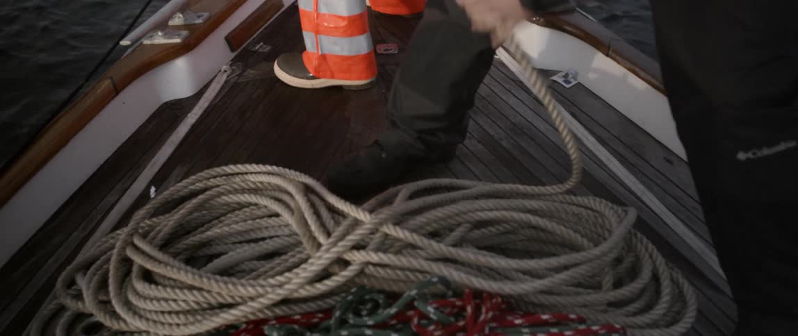 A man on a moving boat is neatly laying out rope
