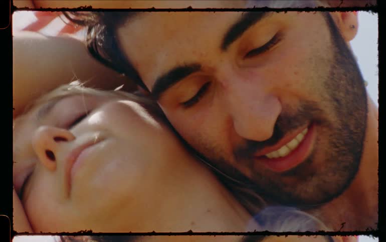 A man and woman smile as they embrace and caress each other while outdoors