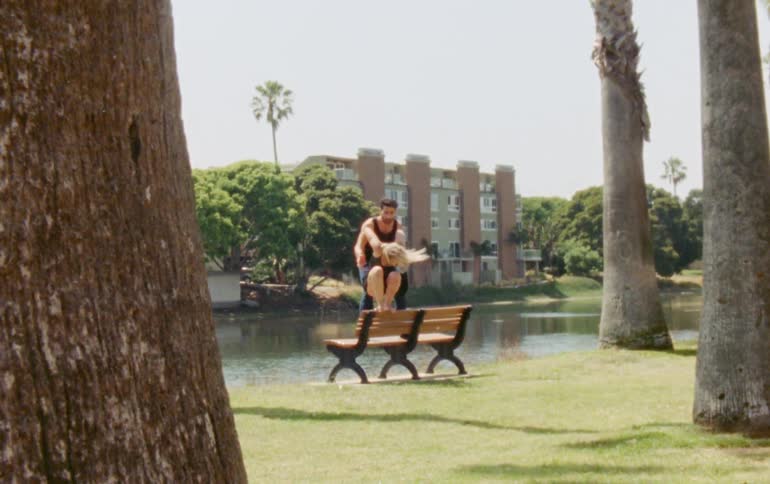A man and a woman dancing on a bench and the woman jumps down to the grass