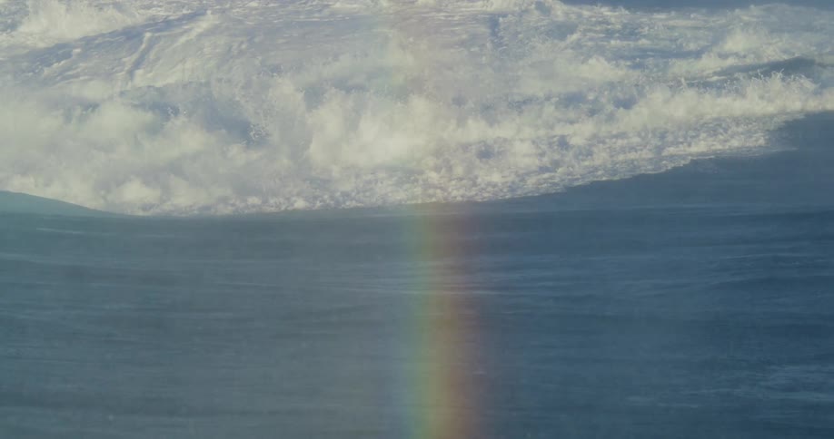 Ocean waves rippling over each other with a rainbow in the mist from the water