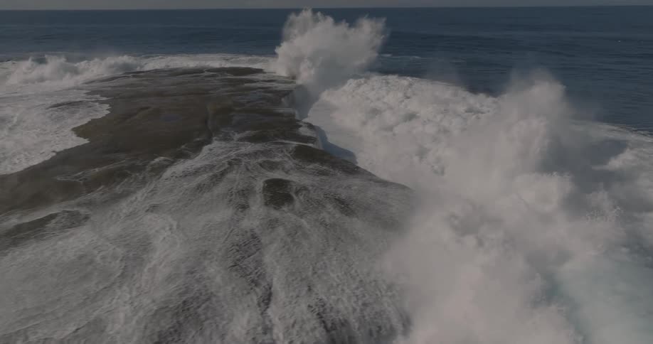 Ocean waves crash over a large flat rocky coast