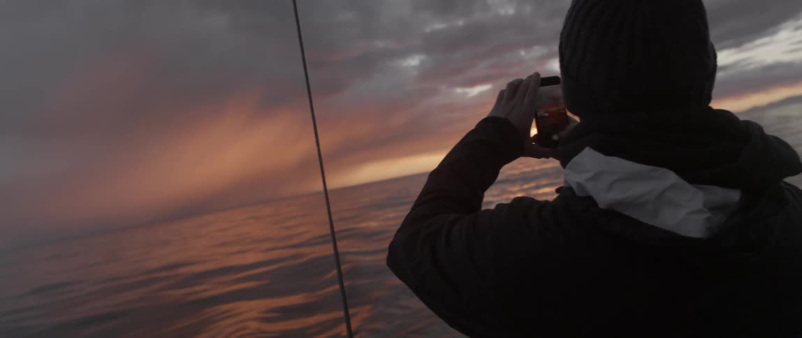 A man is taking photographs from a sailing boat at dawn