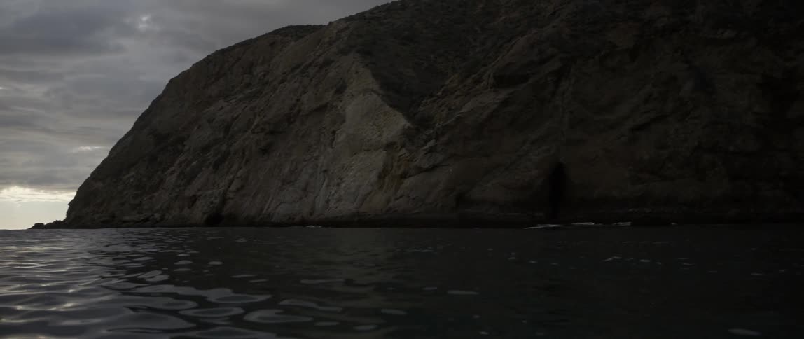 The large rock cliff is surrounded by water