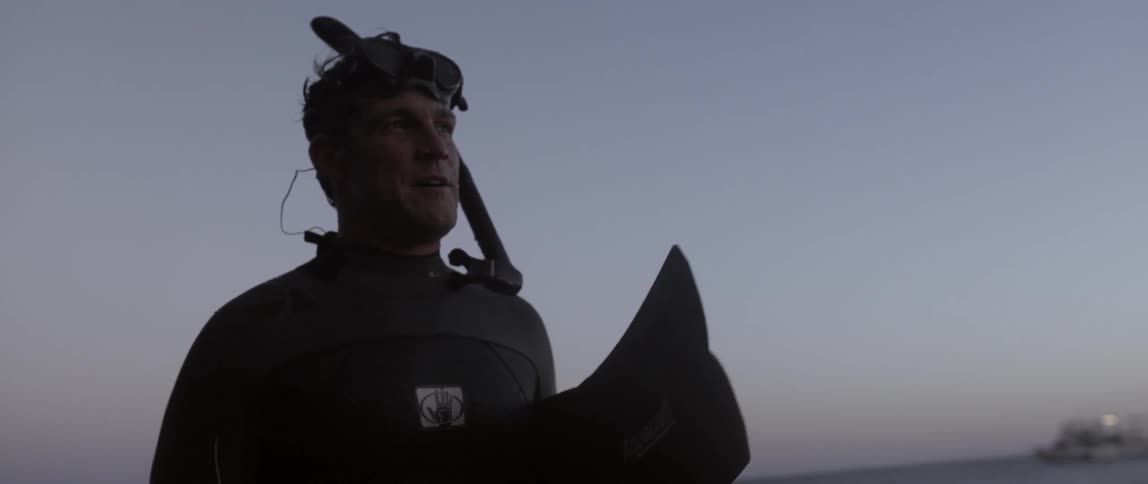 Man wearing a wet suit holding flippers by the beach
