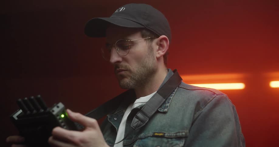 Man wearing a cap operating a remote control in a dimly lit indoor environment