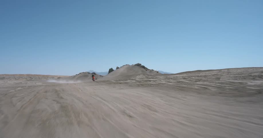 A person practicing motocross at high speed in an arid outdoor environment