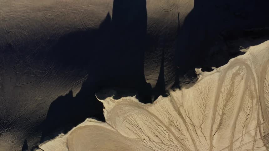 Aerial of mountain crest with sandy slopes on both sides and long shadows