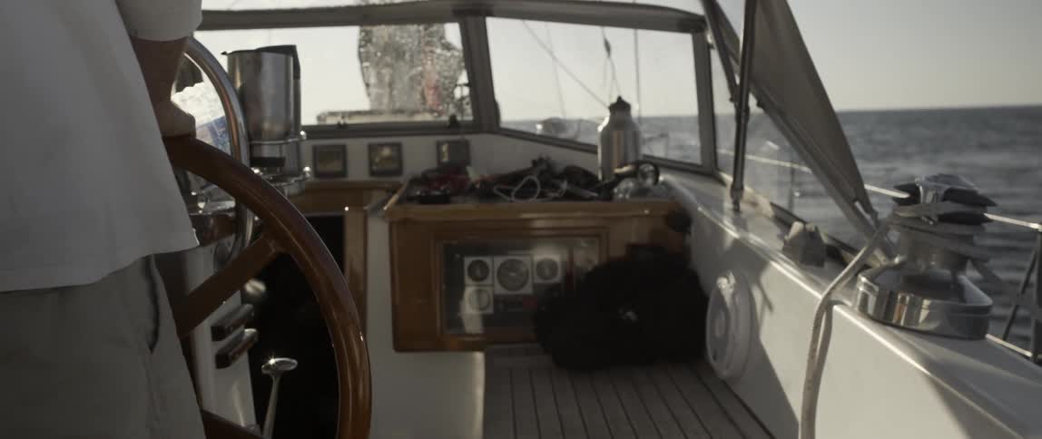 A person is steering the wheel of a boat on a cloudy day