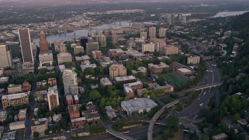 Aerial footage of a bustling metropolis at sunset flying by skyscrapers and Portland State University in downtown Portland Oregon