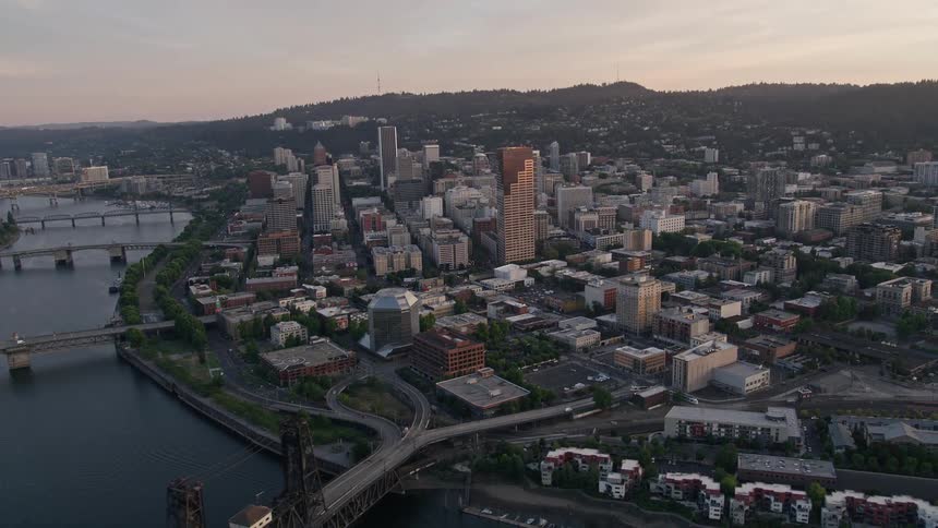 Aerial footage of downtown Portland Oregon at sunset flying over the Willamette River and Steel Bridge