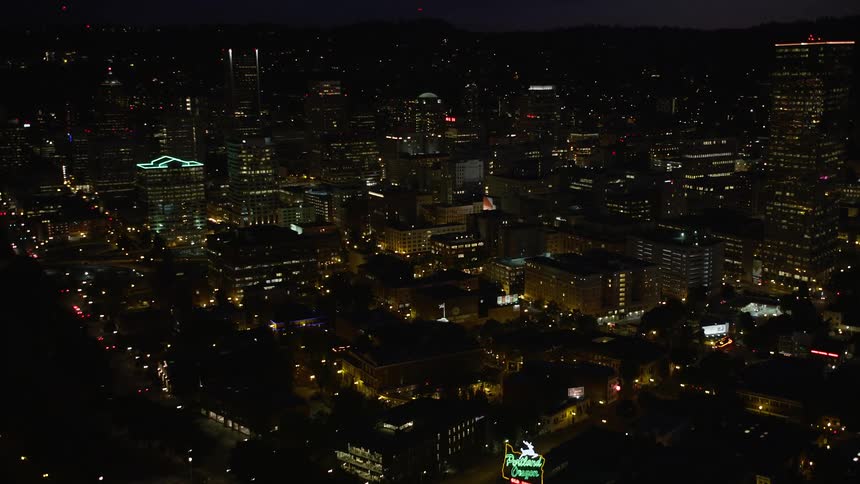 Aerial footage of the Burnside Street Bridge at night approaching downtown Portland Oregon with city lights skyscrapers and the Willamette River in view