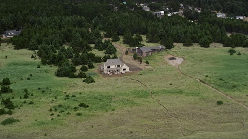 Aerial view of rustic houses surrounded by lush green fields and trees in a rural residential area in Oceanside Washington during a summer day