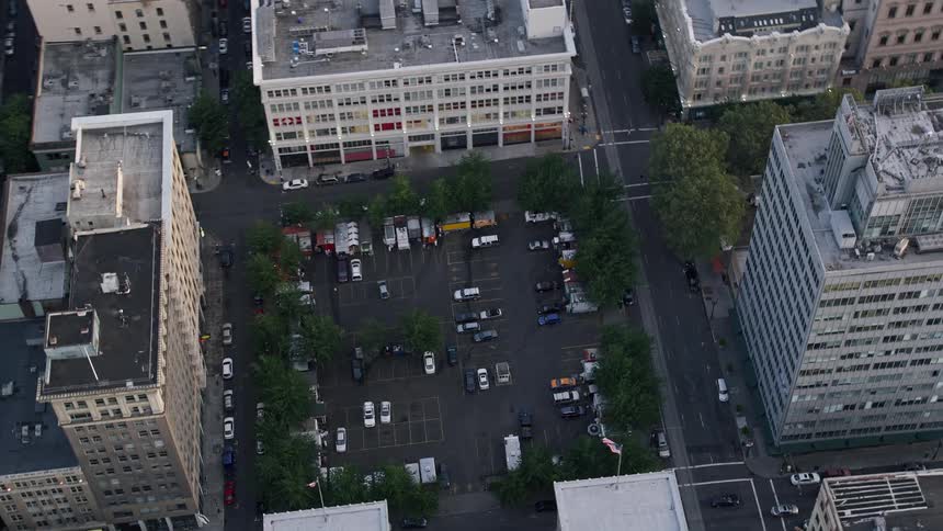 Aerial footage captures the vibrant sunset skyline of Downtown Portland Oregon showcasing a parking lot surrounded by towering office buildings and bustling city streets