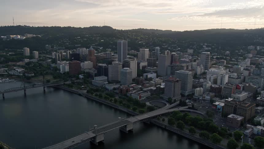 Aerial footage of downtown Portland Oregon during sunset showcasing the Morrison Bridge and city skyscrapers alongside the beautiful Willamette River