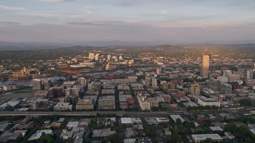 an aerial view of downtown Portland Oregon at sunset showcasing the high-rise buildings the picturesque Willamette River and the captivating Lloyd District all set against a partly cloudy evening sky