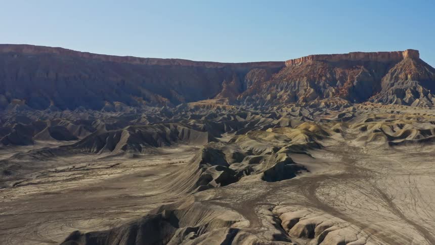 Aerial of hills on the desert next to the mountains under a blue sky