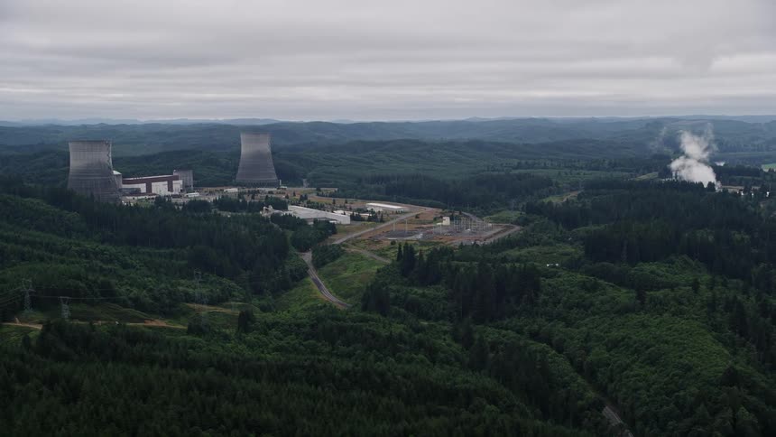 Aerial footage of the Satsop Nuclear Power Plant in Satsop Washington showcasing the power generation facility surrounded by mountains on a sunny summer day