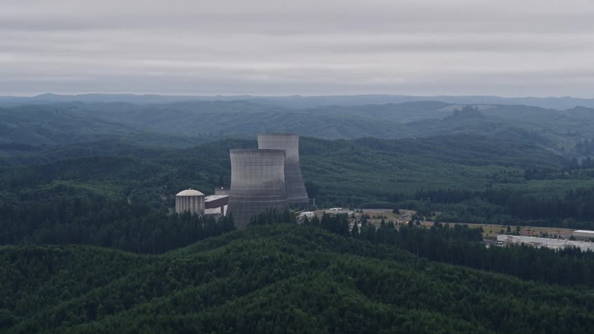 Aerial footage of two cooling towers at the Satsop Nuclear Power Plant in Satsop Washington surrounded by lush forest during a summer day