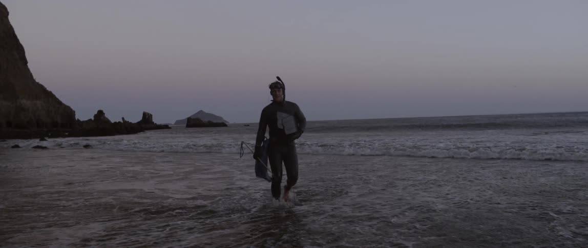 A snorkeler in a wetsuit exits the ocean at dusk
