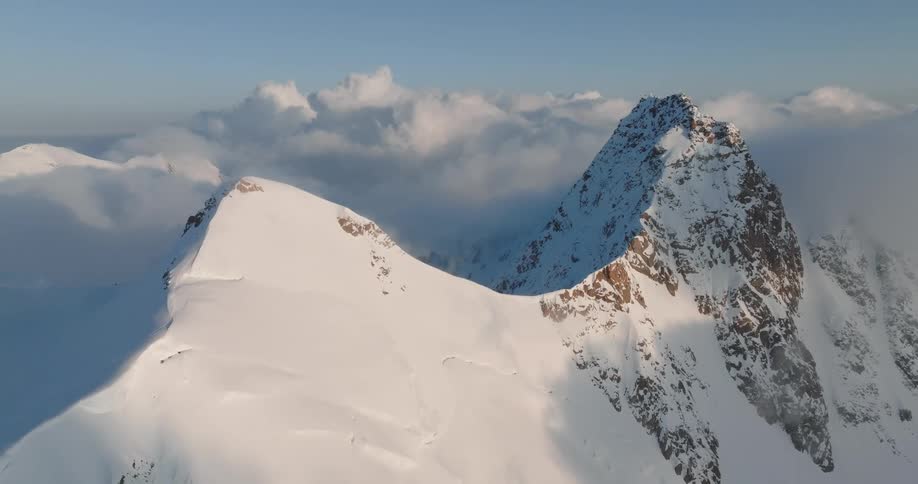 Snow covers twin peaks of mountain towering over clouds
