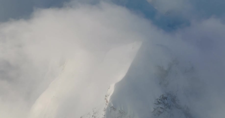 Aerial of the snowcovered ridge of a mountain range under white clouds