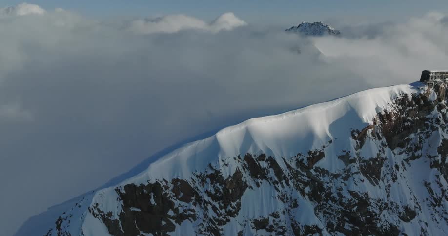 Aerial view of a snowy mountain peak revealing a building at the top