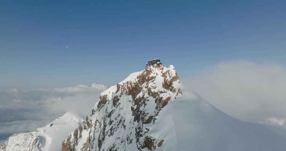 Aerial of a mountain peak covered in snow under a blue sky