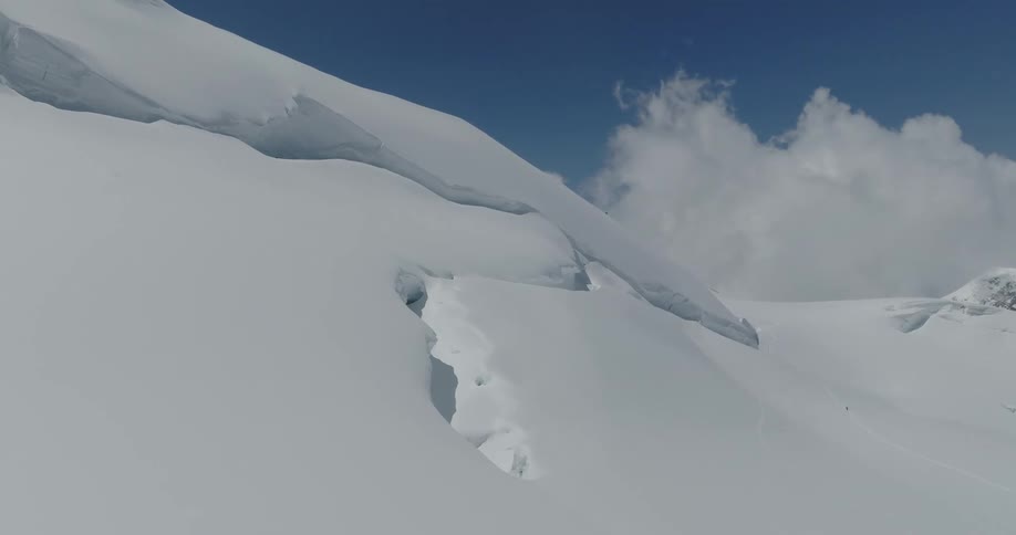 A snow covered mountain with some holes in the snow and in the sky many clouds