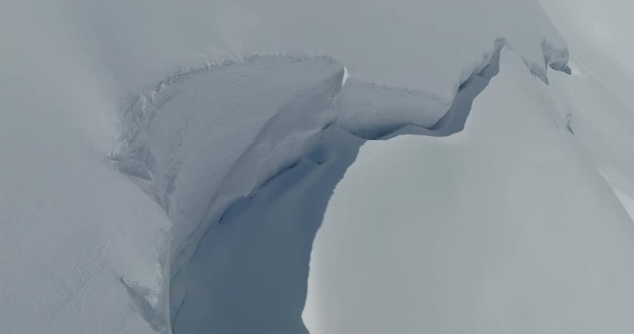 A massive fissure in the surface of a snow covered slope is viewed from above