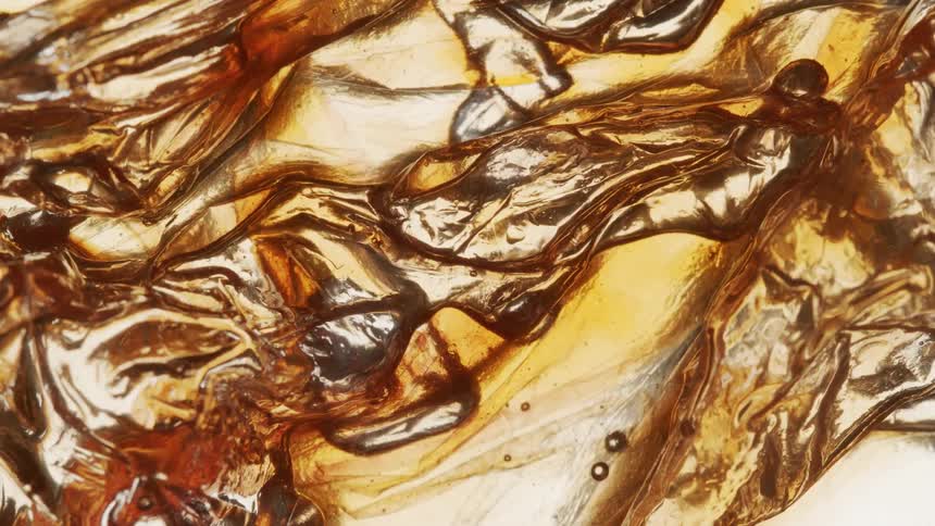 Extreme close up of coagulated liquids with a golden hue in abstract motion