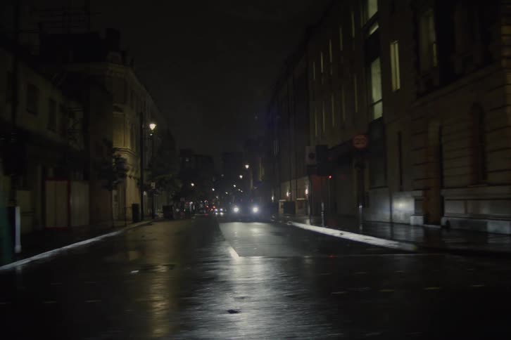At an intersection during the night a car proceeds ahead its tires creating ripples on the wet road surface after a recent rainfall