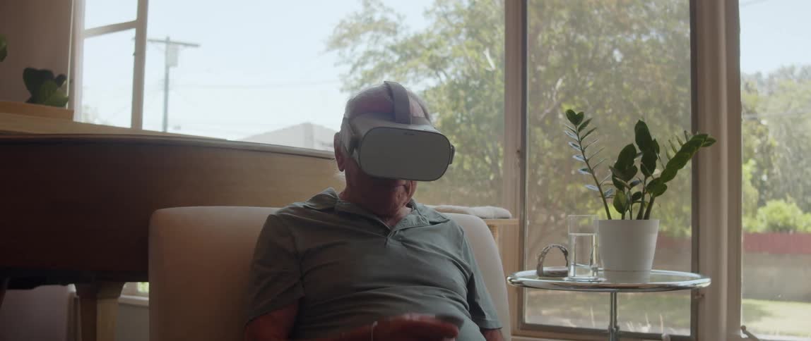 Old man sitting on a chair with a virtual headset attached to his face in daytime