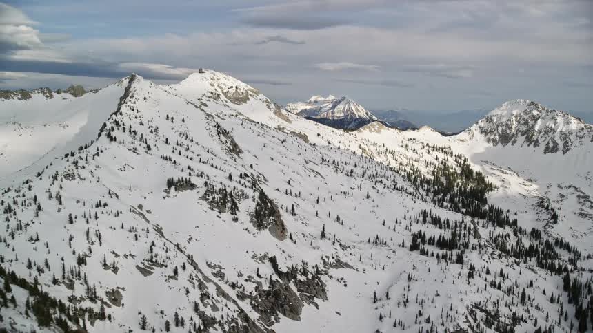  aerial footage pan and approach snow-covered mountains in the Wasatch Range Utah with partly cloudy skies showcasing the winter landscape and natural beauty of the Southwest United States