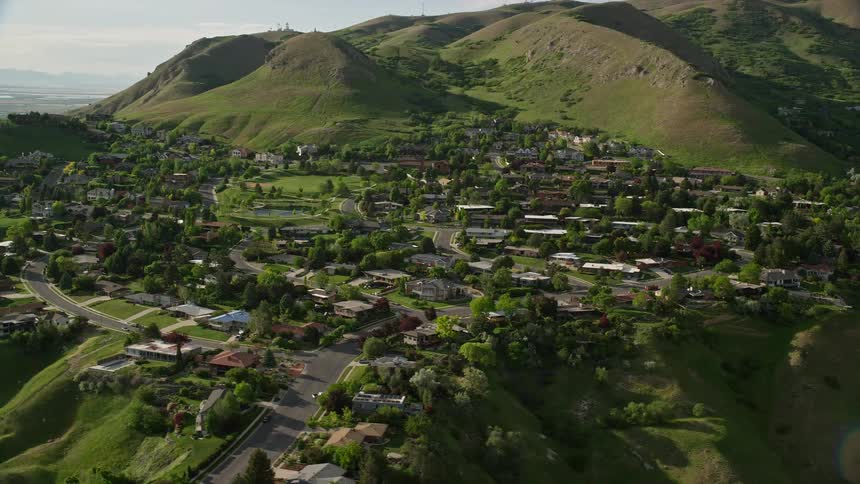  aerial footage of a sunny day flying over a hilltop suburban neighborhood in Salt Lake City Utah with views of the Wasatch Range and misty river valley below