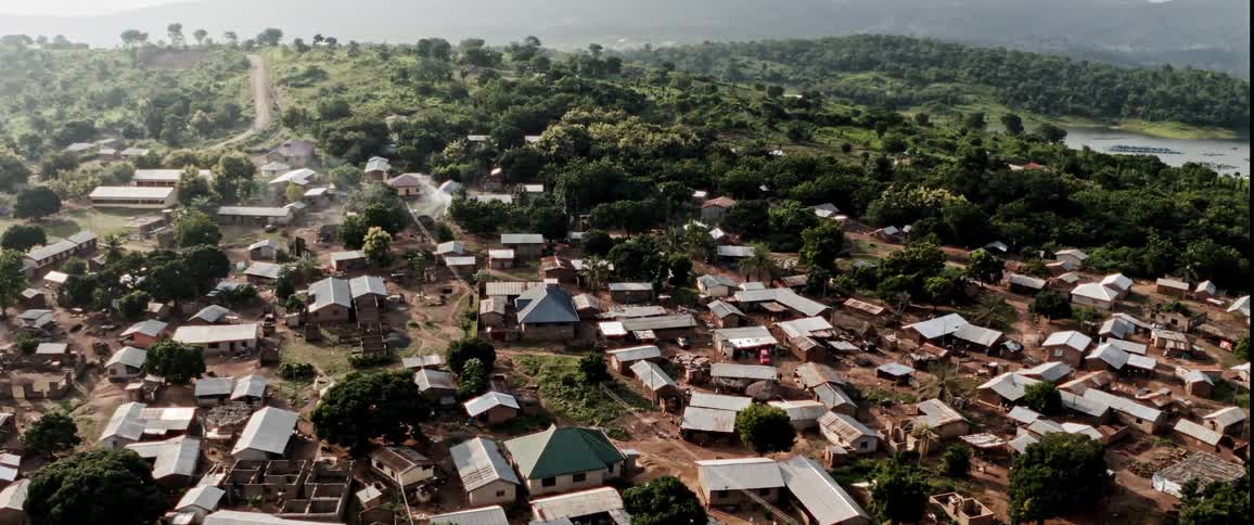 Drone view of a third world village with house structures lined with trees on a bright sunny day