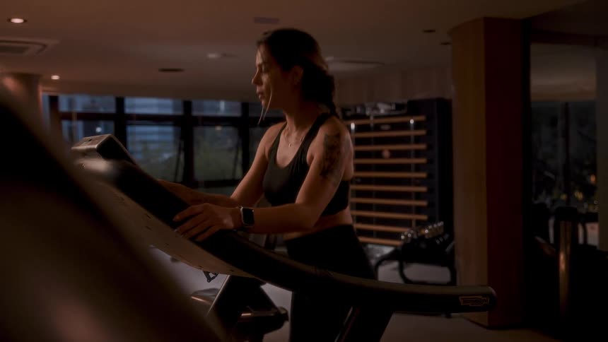 A woman exercises on a treadmill indoors in the evening
