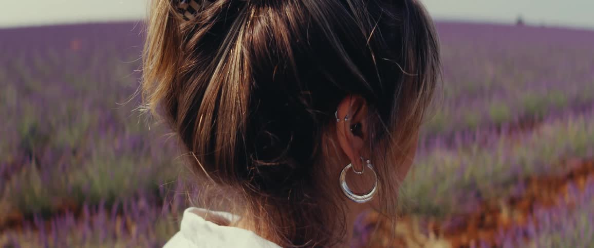 Close up of a womans head as she looks out over a purple flowering field during the day