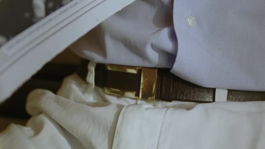 A golden belt buckle on a brown belt worn with white pants and blue shirt