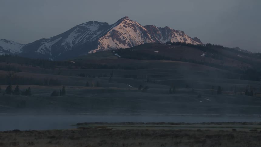 Snow capped mountains hover over a vast open field