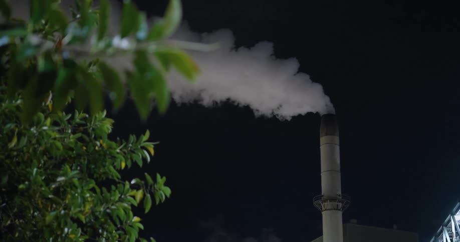 Closeup of a factory with a chimney releasing smoke during the night