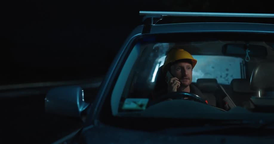 Man sitting in the car talking on the phone and removing his protective helmet
