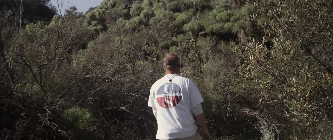 A man is walking towards a hill covered with bushes