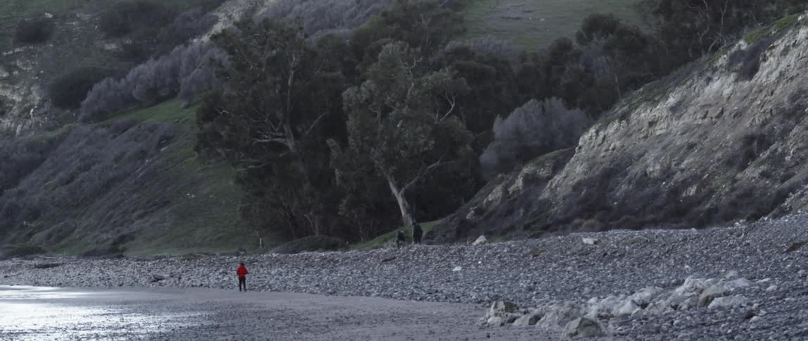 A person is walking in the distance by the rocks on a shore