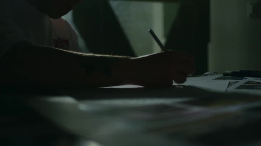 Person writes on paper at table in dim room
