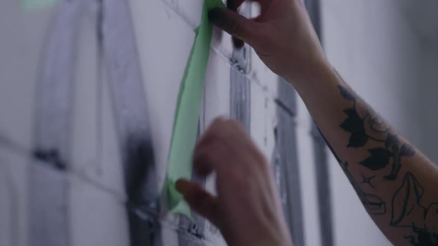 A man is putting painters tape on the wall