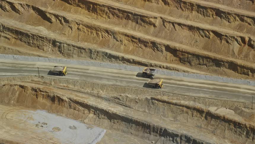  aerial footage of gravel haulers in Kennecott Copper Mine Utah as they transport sand and stone along a dirt road during a hot summer day amidst partly cloudy skies