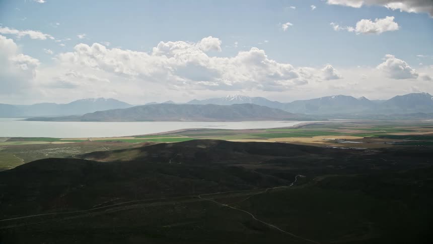 A stunning high-definition aerial footage capturing the scenic views of farmland distant mountain range and Utah Lake in Utah with partly cloudy skies and a rustic rural landscape