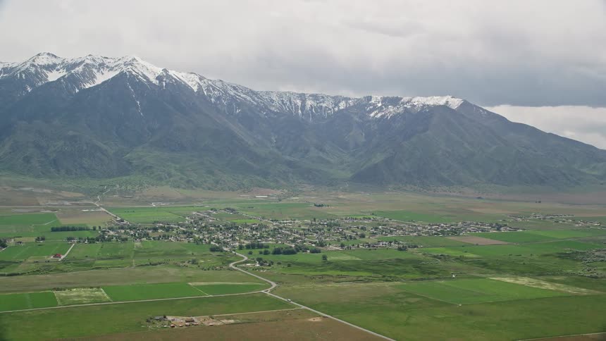 Aerial view of a small rural town nestled in a valley beneath snow-covered mountains in Mona Utah during a cloudy day