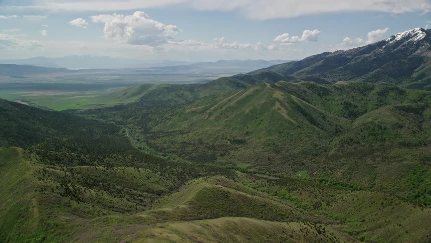 an aerial view of the lush green slopes and snow-covered peaks of the Oquirrh Mountains in Utah during summer