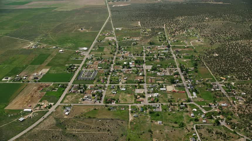 Aerial view of a rural residential area surrounded by agricultural land and mountains in Cedar Fort Utah on a partly cloudy day